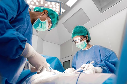 Un médico y una enfermera con instrumentos quirúrgicos en las manos haciendo una operación, en una sala operatoria.