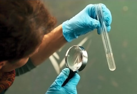 Left side is a person with a magnifying glass inspecting liquid in cylinder
