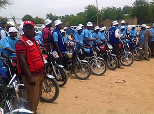Community health workers on motorcycles get ready to travel to different villages, where they will distribute the oral cholera vaccine door-to-door. Because the vaccine must stay cold, they are carrying it in small coolers