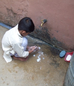 A boy in the developing world washing his hands with soap under an outdoor tap.