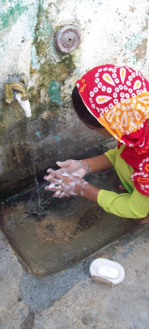 A girl in Pakistan washing her hands with soap under an outdoor tap.