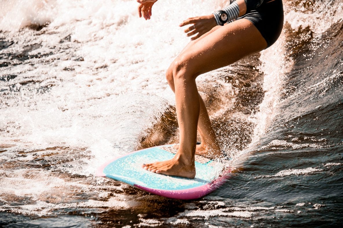 close-up of athletic legs of young woman riding wave on surf style wakeboard