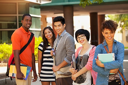 A group of five smiling diverse outside of a school