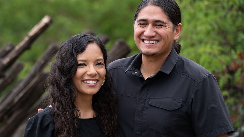 A smiling Native American couple dressed in black shirts.