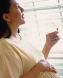 Prgnant woman holding a glass and looking out a window.