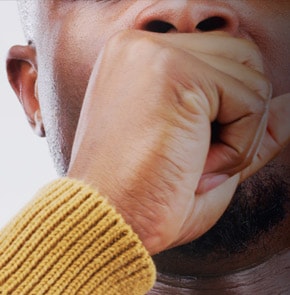 Close-up of a man coughing into fist.