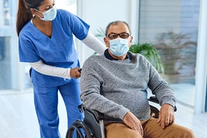 Woman in scrubs pushes an elderly gentleman in wheelchair