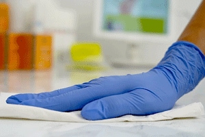 hand with a blue glove wipes a counter top