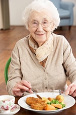 PHot of an elderly woman smiling and eating supper.