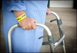 The figure above is a photograph showing an older man using a walker with a yellow 'fall risk' bracelet on his wrist.