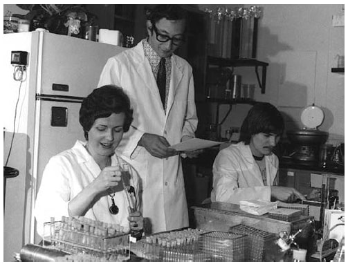 Figure is a photo of laboratorians checking serologic tests for swine flu in 1976.