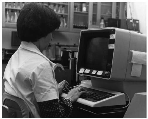 The figure is a photo of a CDC employee at a computer workstation in the 1980s.