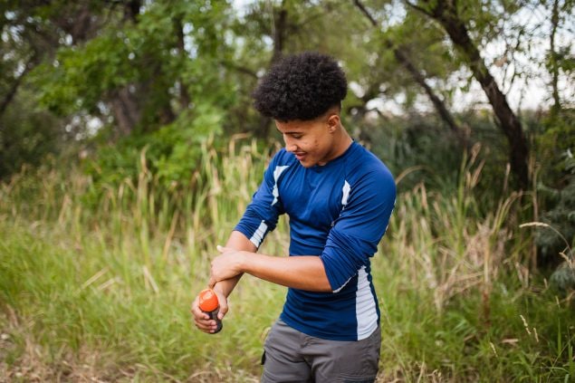 Teenager applying insect repellent to protect himself from mosquito bites
