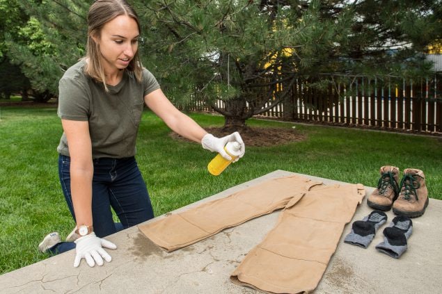 Photo of a woman applying permethrin to her pants and outdoor clothing.