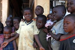 This photograph shows a group of young African children standing side by side. A few are looking at the camera and smiling while others are looking to the side.