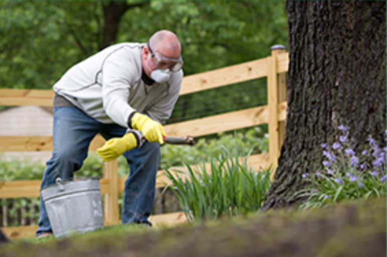 A man working outdoors wearing rubber gloves, goggles, and a mask