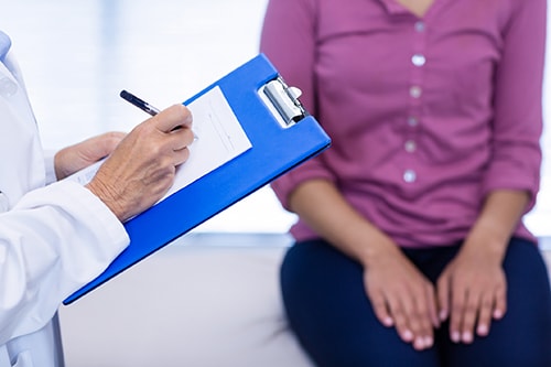 Female doctor writing on clipboard in clinic with female patient