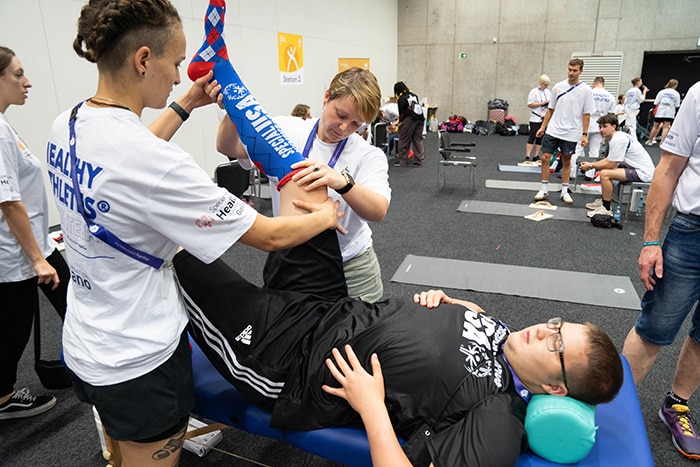 Dos entrenadores ayudando a un deportista de los Juegos Paralímpicos a hacer estiramiento.
