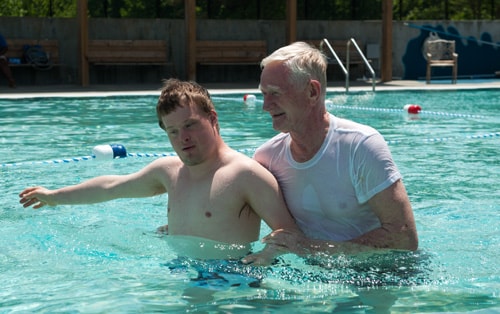 Boy with Down Syndrome in a pool with a man helping him.
