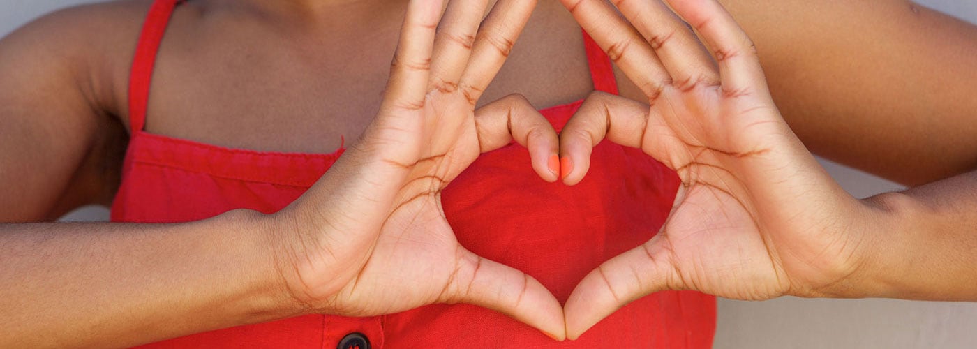 Woman making a heart sign with fingers over her heart and smiling