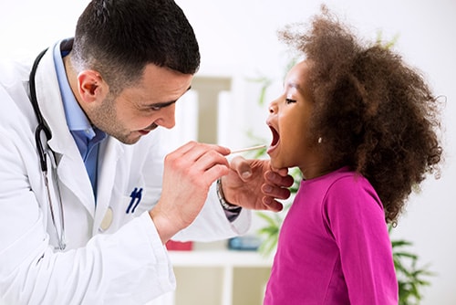 Doctor looking in a young girls mouth with a tongue depressor