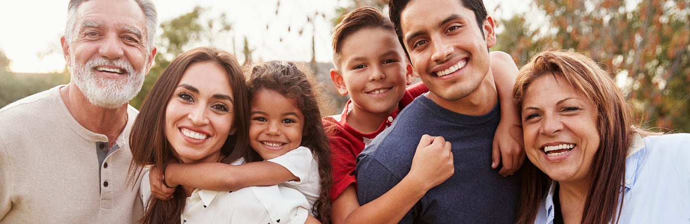 Tres familia de hispano de generación que está de pie en el parque que sonríe a cámara