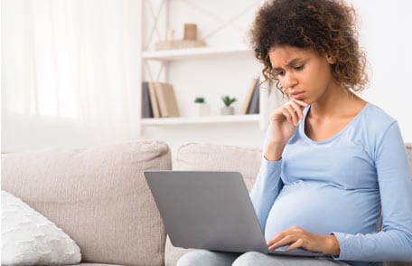 A pregnant woman looking at a laptop computer.