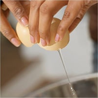 Photo of hands breaking open an egg.