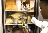 Woman taking temperature of food in refrigerator.