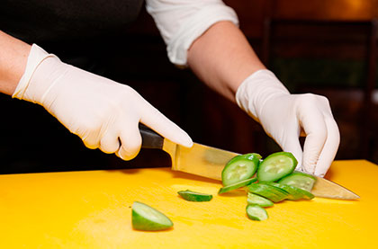 A chef wearing sanitary gloves cutting a cucumber with a knife