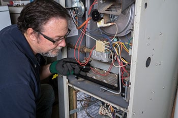A man holding a flashlight while inspecting inside of a home furnace