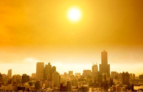 A blazing sun and hazy sky above a large city skyline.
