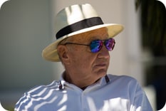 Older man wearing hat and sunglasses sitting in shade