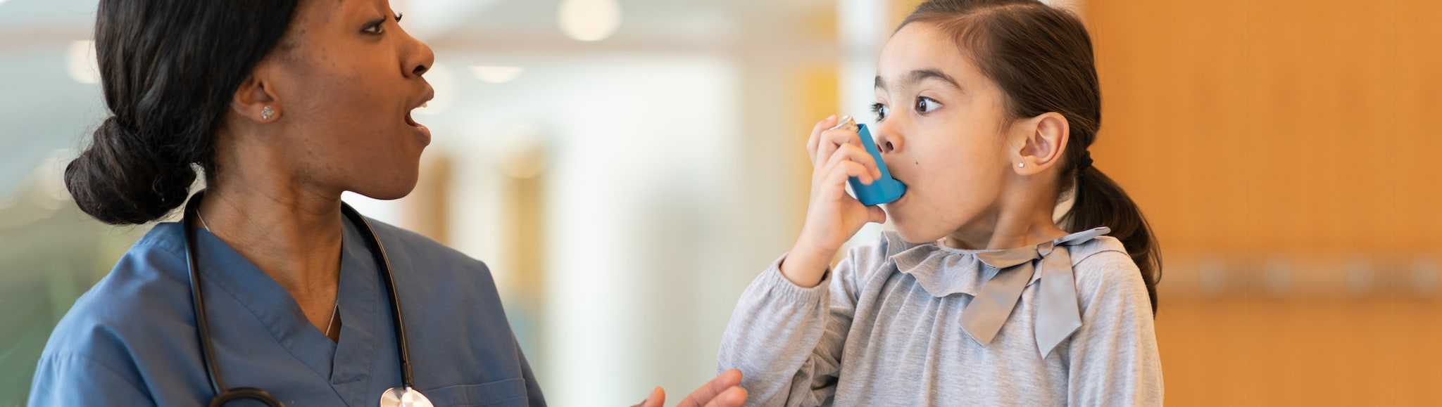 Doctor supervises young girl using asthma inhaler