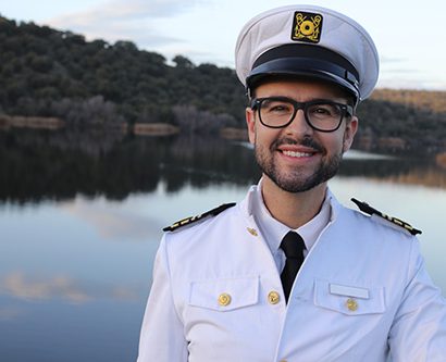 Ship captain in white uniform with body of water in the background.