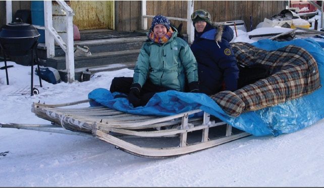 CDC scientists in heavy coats sitting with their equipment on a dog sled 