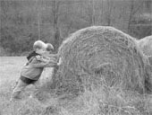 two children pushing against a round bale of hay