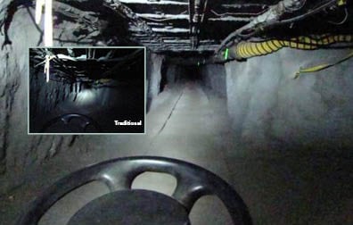 This photo shows a mining tunnel. The ceiling is gridded with what looks like a system of steel pipes and bars. Running along the right side is a yellow tube. The picture is taken from the perspective of a rail car driving down the tracked tunnel—as evidenced by the top third of a steering wheel at the bottom center of the picture. Inset is another picture (labeled before) of the same scene. Most of the ceiling and walls are in complete darkness. One bright spot of light illuminates a small part of the tunnel directly in from of the rail car.