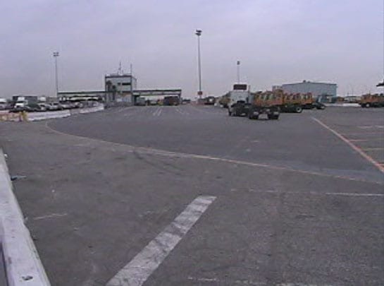 Exhibit 4. A picture of the incident scene looking east. The forklift parking area is on the right of the picture. The employee parking lot is on the left of the picture. The top handler was headed to the area on the left of the picture.