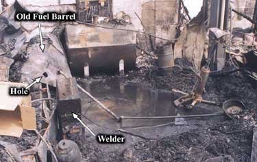 Photo 1 – View of the burned out shop area, showing the old fuel barrel and welder.
