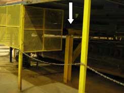 Arrow shows the horizontal crossbeam under the stacker, inside the barricaded area.