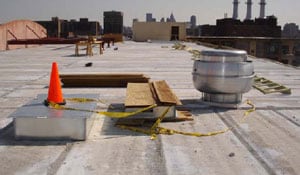 Figure 1. Make-up air roof curb with orange pylon, exhaust fan roof curb with plywood, looking south on roof.