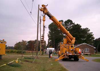 A boom truck with an auger attached was turning a utility pole anchor in an anchor-setting process.