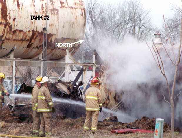Photo 2: Photograph of the south side of Tank #1 prior to the explosion, showing fire fighters applying water to the tank's surface.
