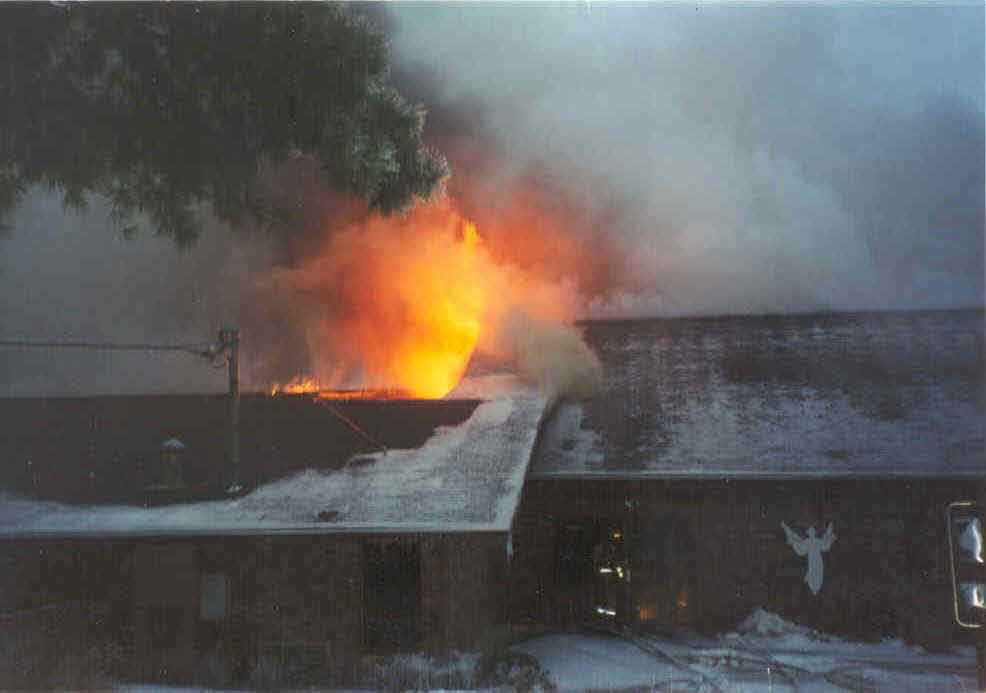 Structure while fully involved, showing doors where crews entered and also showing fire venting over collapsed area of building.