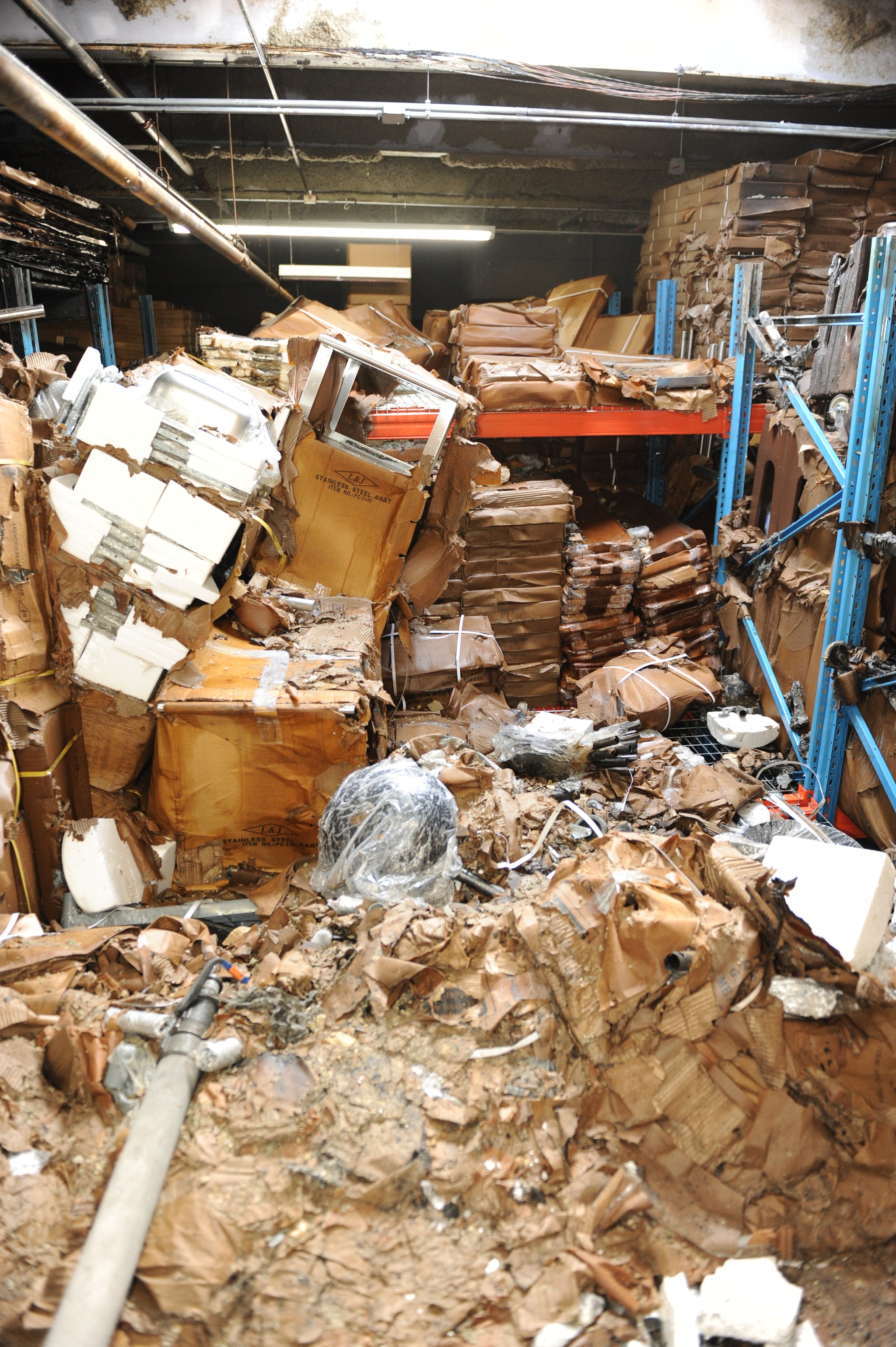 The fire area contains cardboard boxes damage by the fire and water used to suppress the fire.  Many of the cardboard boxes have fallen off the storage racks and broken open revealing plastic shelving and restaurant equipment.