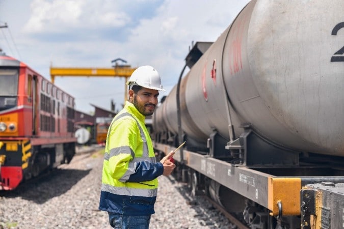 man in safety vest and hard hat standing next to railway cars.