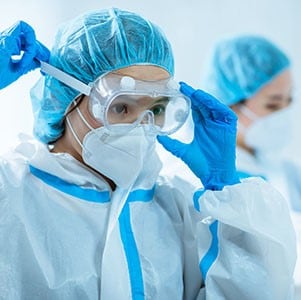 Healthcare workers suiting up with personal protective gowns, caps, and gloves putting protective eyewear on.