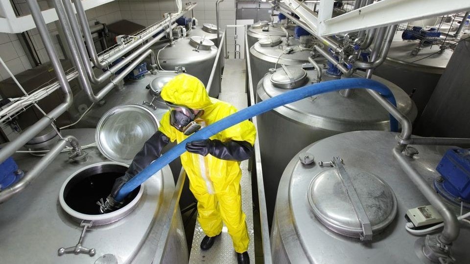 chemical manufacturing worker in a yellow suit handling chemicals in a large steel canister
