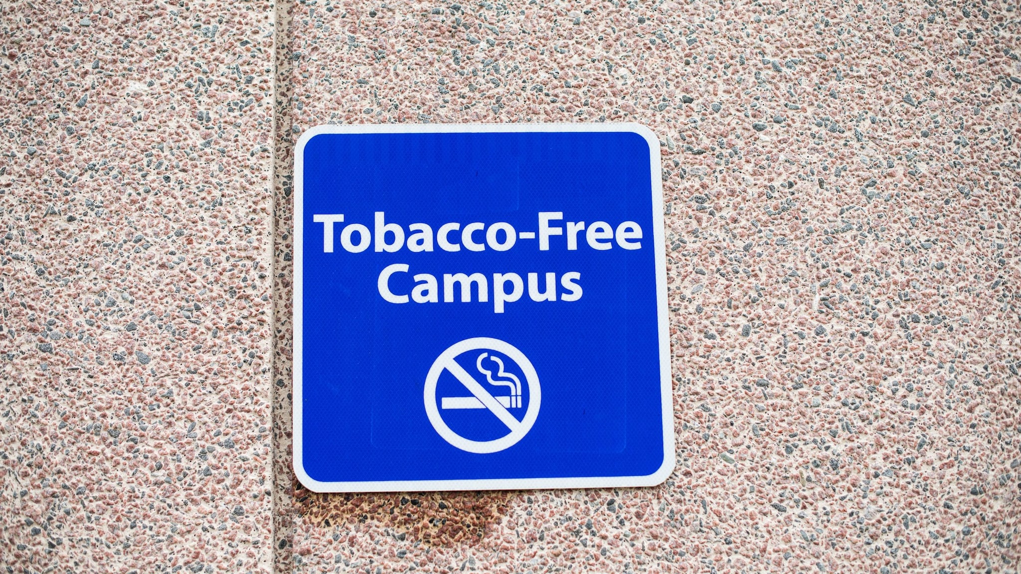 A tobacco-free campus sign hanging on a stone wall.